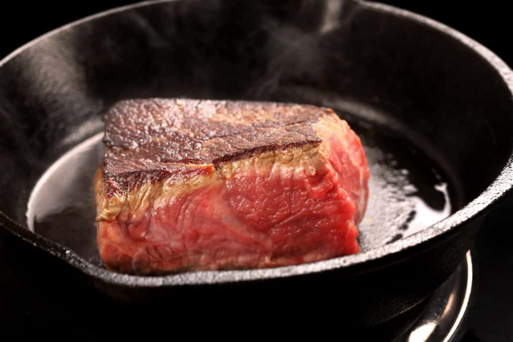Close up of steak being seared in cast iron pan